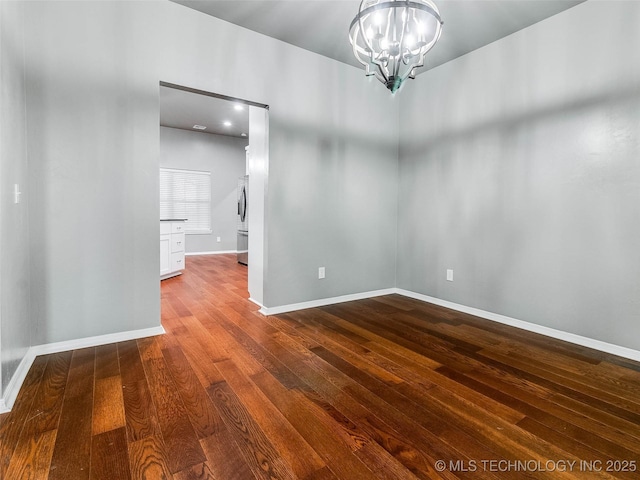 spare room with a notable chandelier, baseboards, and dark wood-style flooring