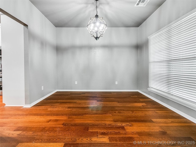 empty room with a chandelier, visible vents, baseboards, and wood finished floors