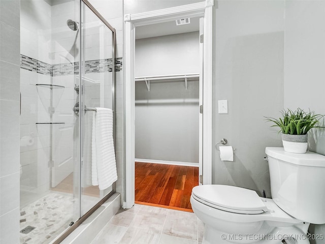 bathroom featuring wood finished floors, visible vents, a stall shower, a spacious closet, and toilet