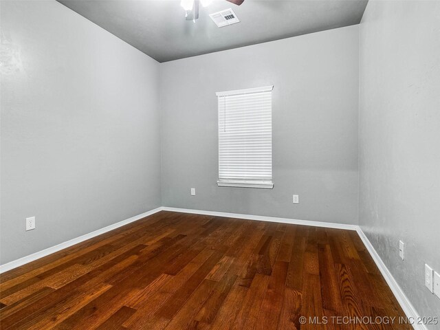 spare room featuring ceiling fan, visible vents, baseboards, and dark wood finished floors