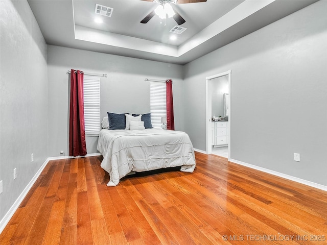 bedroom featuring a tray ceiling, visible vents, and wood finished floors