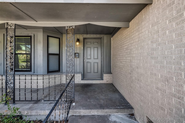 view of exterior entry featuring brick siding and covered porch