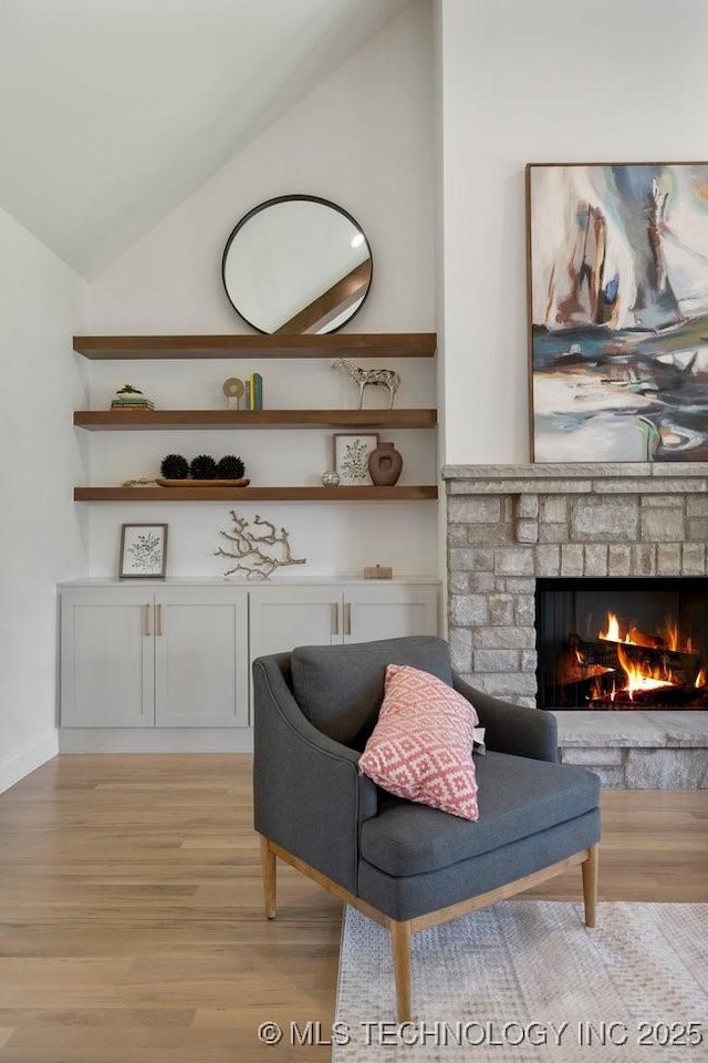 living area featuring a stone fireplace, light wood-style flooring, and vaulted ceiling