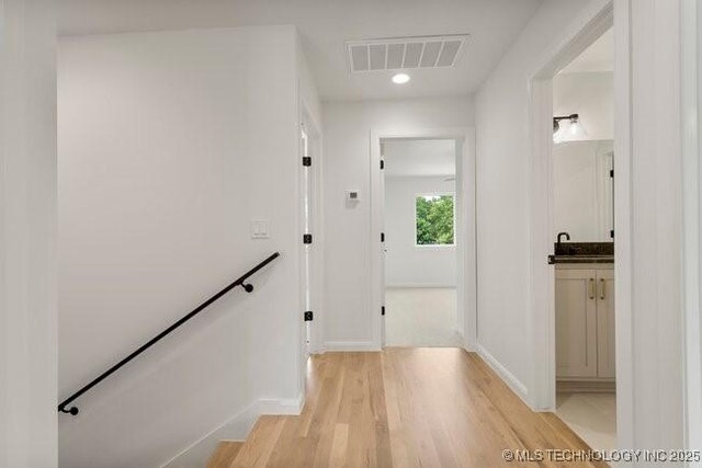 hallway with baseboards, an upstairs landing, visible vents, and light wood-type flooring