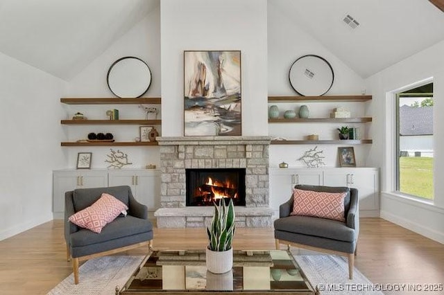 interior space with visible vents, high vaulted ceiling, wood finished floors, a stone fireplace, and baseboards