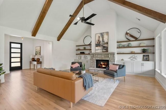 living area featuring a stone fireplace, beam ceiling, light wood-style floors, and a ceiling fan