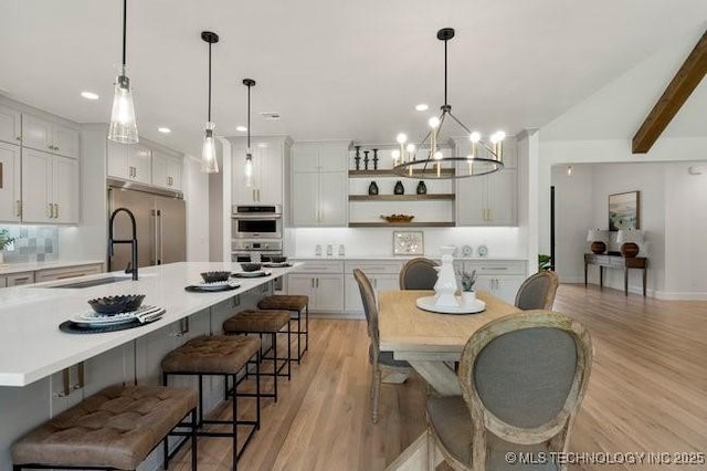 dining room with a chandelier, beamed ceiling, recessed lighting, and light wood-style floors