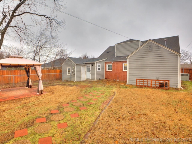 rear view of property featuring a gazebo, a fenced backyard, brick siding, and a patio area