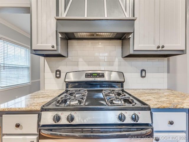 kitchen featuring tasteful backsplash, light stone countertops, gas range, ornamental molding, and wall chimney exhaust hood