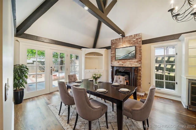 dining space with a chandelier, beam ceiling, a fireplace, french doors, and wood finished floors