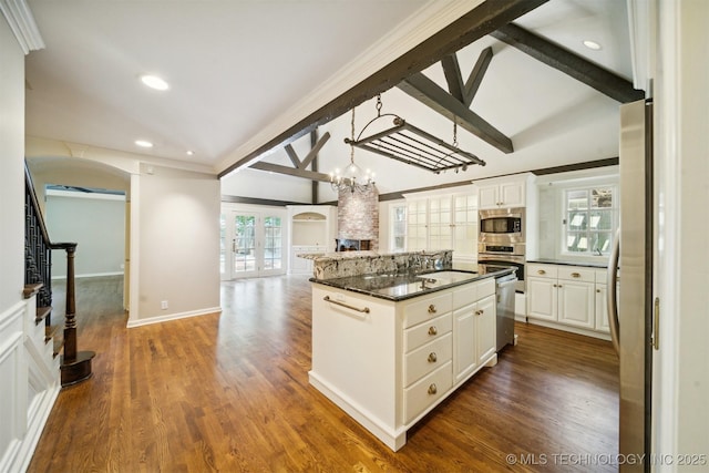 kitchen with lofted ceiling with beams, arched walkways, appliances with stainless steel finishes, and open floor plan