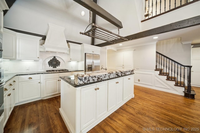 kitchen with custom range hood, dark wood finished floors, appliances with stainless steel finishes, white cabinets, and a towering ceiling