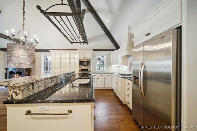 kitchen with a brick fireplace, lofted ceiling with beams, custom range hood, stainless steel appliances, and a sink