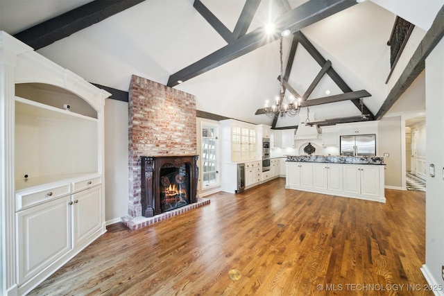 unfurnished living room with beamed ceiling, wood finished floors, wine cooler, a brick fireplace, and a chandelier