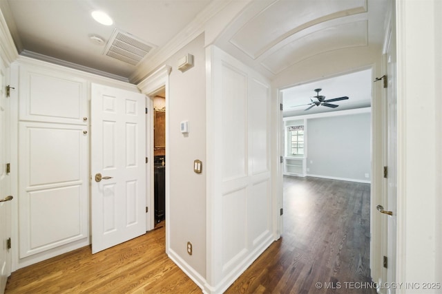 corridor featuring visible vents, baseboards, light wood-style floors, and ornamental molding