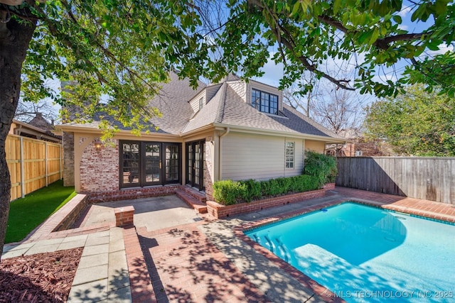 rear view of property featuring a fenced in pool, a fenced backyard, a shingled roof, a patio area, and brick siding