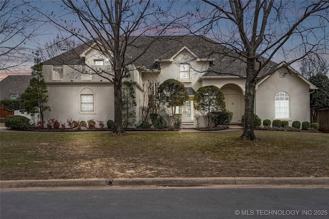 french country inspired facade with stucco siding and a front yard