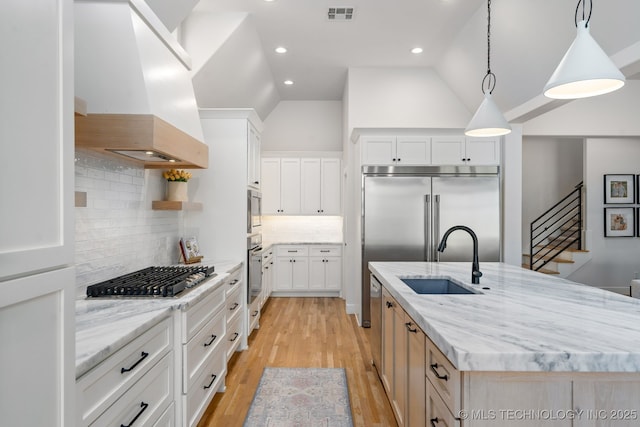 kitchen with ventilation hood, visible vents, a kitchen island with sink, a sink, and appliances with stainless steel finishes