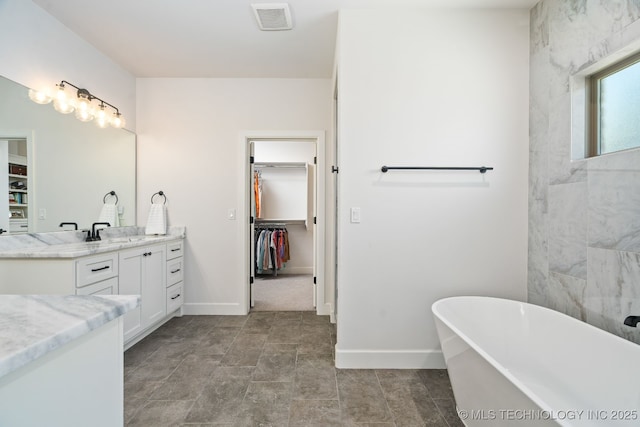 full bathroom with visible vents, a walk in closet, baseboards, a freestanding bath, and vanity