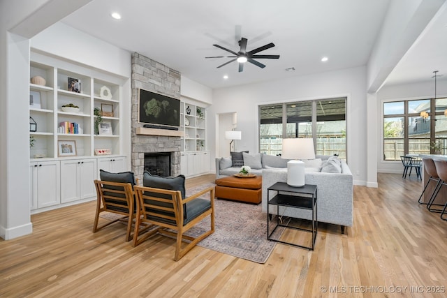 living room featuring a stone fireplace, ceiling fan with notable chandelier, light wood-style floors, and recessed lighting