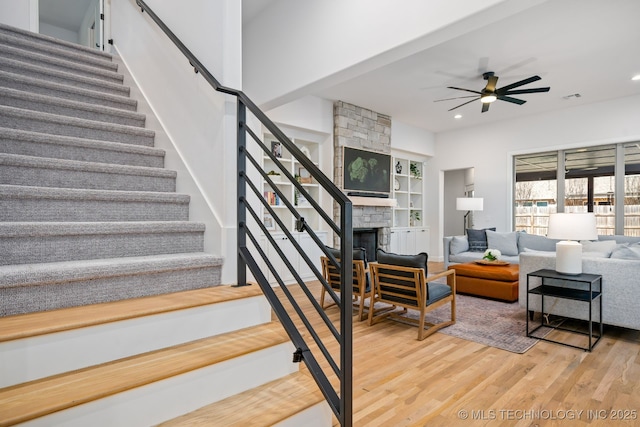 stairs with wood finished floors, visible vents, recessed lighting, ceiling fan, and a stone fireplace