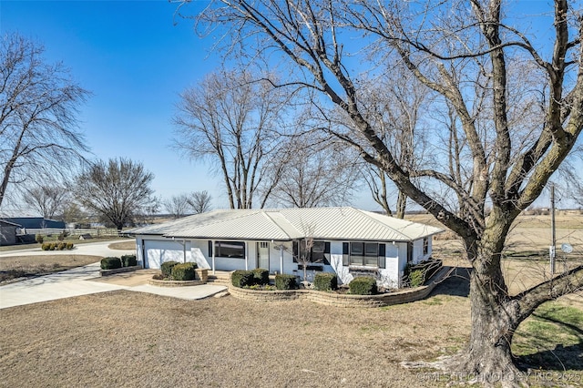 ranch-style home with an attached garage, concrete driveway, and metal roof