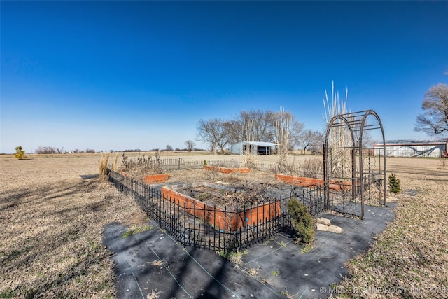 view of yard with a rural view, a vegetable garden, an outdoor structure, and fence