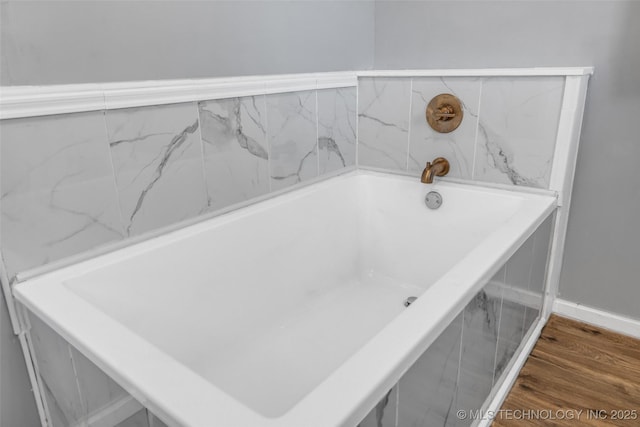 full bath featuring wood finished floors, a tub to relax in, and baseboards