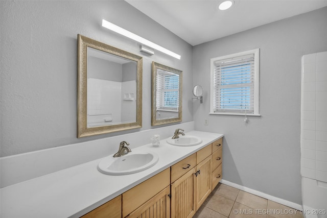 full bath with tile patterned flooring, double vanity, baseboards, and a sink