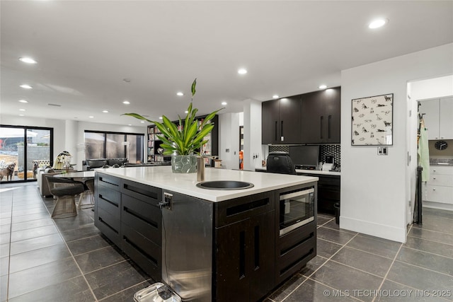 2440 E 47th Pl, Tulsa, OK 74105 - kitchen with stainless steel microwave, backsplash, dark tile patterned floors, light countertops, and recessed lighting
