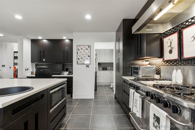 2440 E 47th Pl, Tulsa, OK 74105 - kitchen featuring wall chimney range hood, stainless steel appliances, light countertops, dark cabinetry, and backsplash