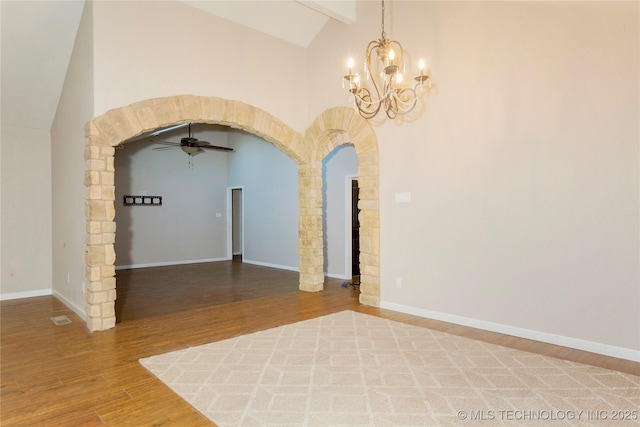 unfurnished room featuring baseboards, beam ceiling, ceiling fan with notable chandelier, wood finished floors, and arched walkways