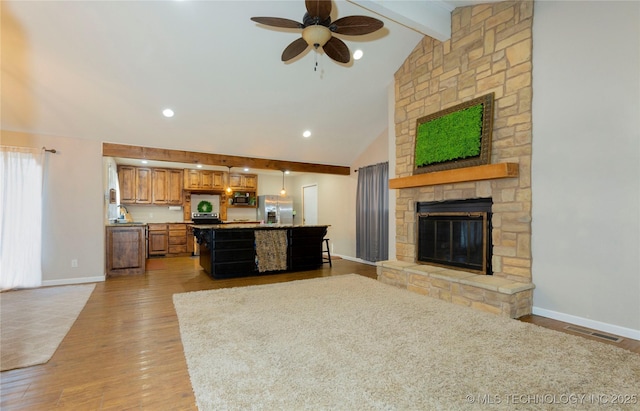 living area with visible vents, beamed ceiling, light wood-style flooring, a fireplace, and baseboards