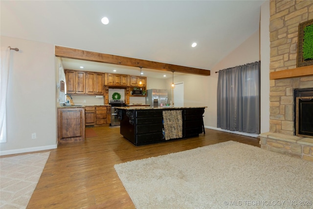 kitchen featuring beam ceiling, stainless steel appliances, light wood-style floors, a stone fireplace, and brown cabinetry