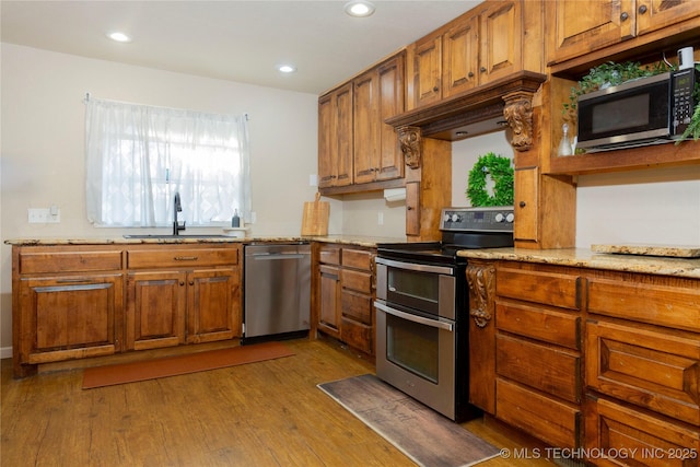 kitchen with brown cabinetry, wood finished floors, stainless steel appliances, and a sink