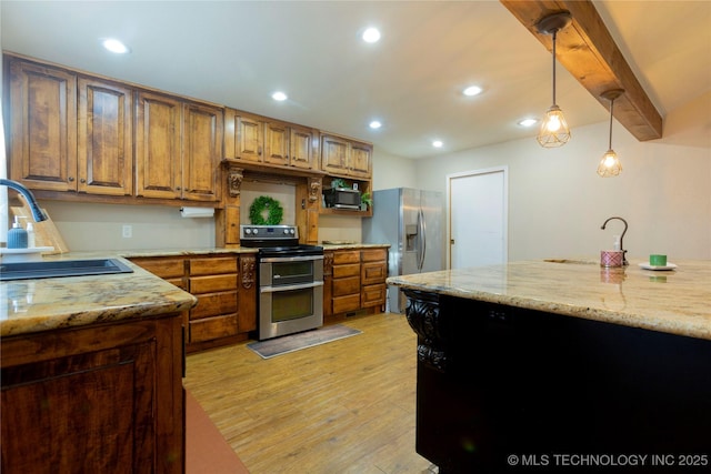 kitchen featuring light stone countertops, a sink, light wood-style floors, appliances with stainless steel finishes, and decorative light fixtures