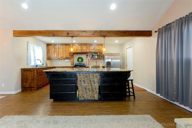 kitchen featuring an island with sink, a sink, stainless steel appliances, dark wood-type flooring, and beamed ceiling