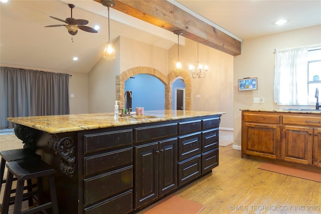 kitchen with a kitchen bar, light stone counters, lofted ceiling with beams, a sink, and light wood finished floors