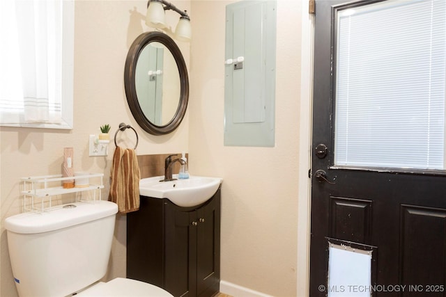 bathroom featuring electric panel, toilet, vanity, and baseboards