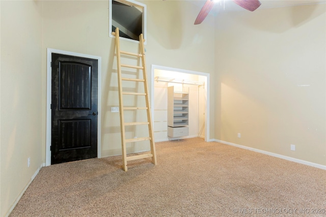 interior space featuring a high ceiling, carpet flooring, a ceiling fan, and baseboards