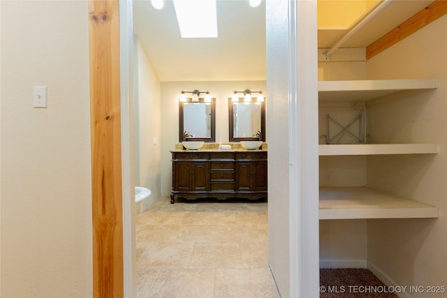 full bathroom featuring double vanity, a skylight, and a sink