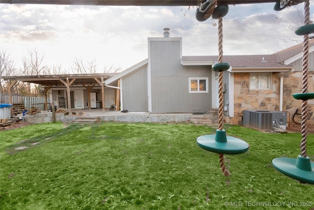 back of house with cooling unit, a chimney, stone siding, a patio area, and a lawn