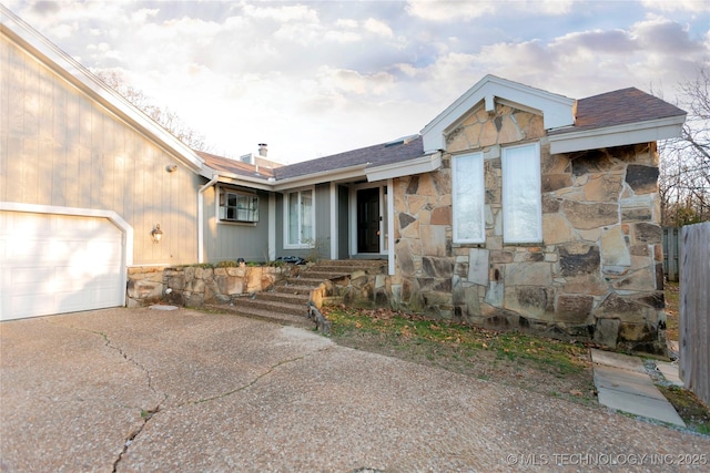 view of front facade featuring stone siding, an attached garage, a chimney, and concrete driveway