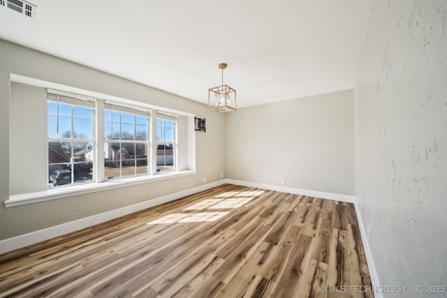 spare room featuring a notable chandelier, visible vents, baseboards, and wood finished floors