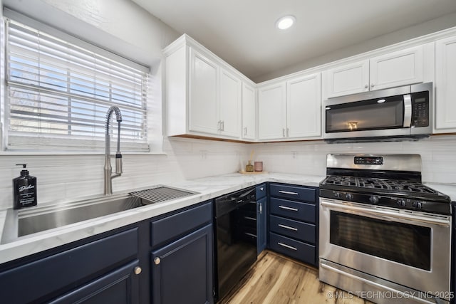 kitchen with a sink, blue cabinetry, tasteful backsplash, white cabinetry, and stainless steel appliances