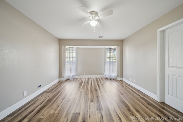 empty room featuring ceiling fan, visible vents, baseboards, and wood finished floors