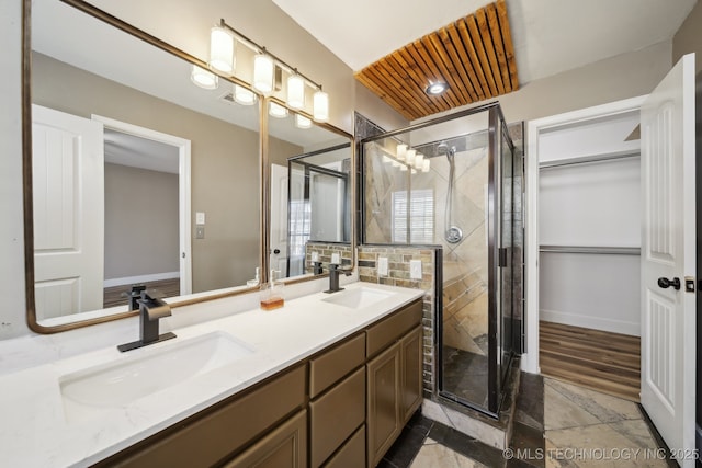 full bathroom featuring double vanity, a shower stall, a walk in closet, and a sink