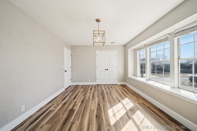 unfurnished dining area with visible vents, baseboards, wood finished floors, and a chandelier