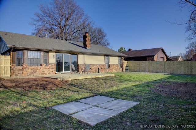 rear view of house with stone siding, a lawn, a chimney, and fence