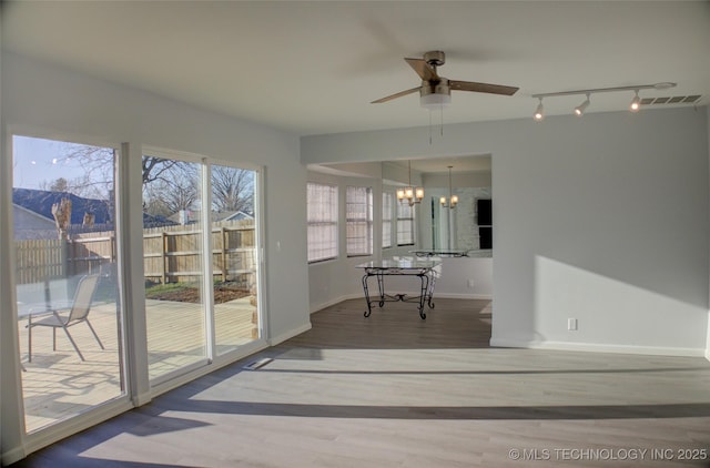 unfurnished sunroom featuring rail lighting, ceiling fan with notable chandelier, and visible vents